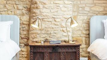 A bedroom with a stone wall, a wooden nightstand, two bedside lamps, and striped bedding.