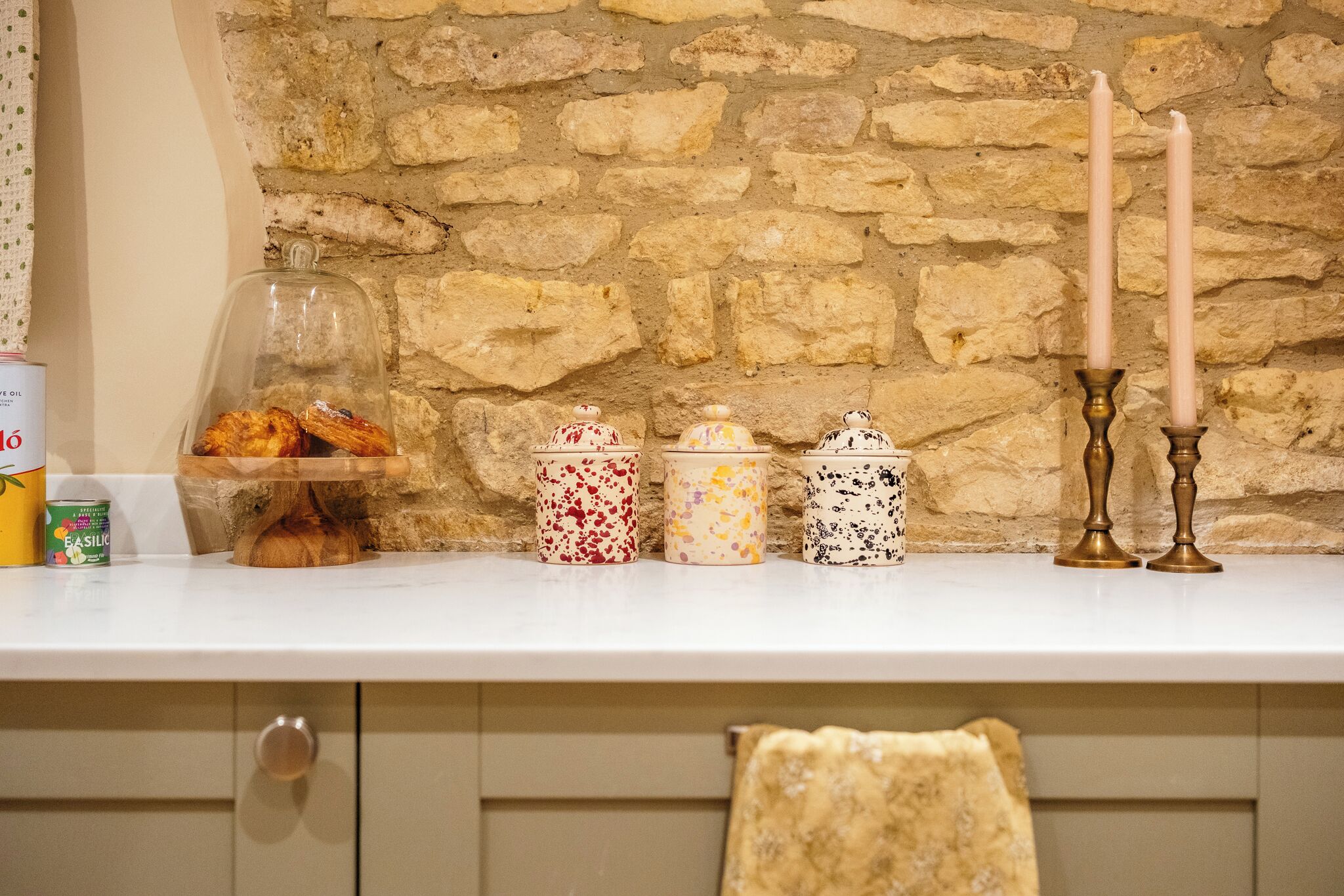 A kitchen counter with a stone wall background, a glass display case with pastries, and decorative jars.