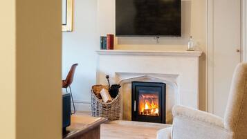 Een woonkamer met een open haard, een televisie erboven en een comfortabele fauteuil.
