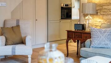 A living room with a sofa, a table with plates and glasses, a lamp, and a kitchen in the background.