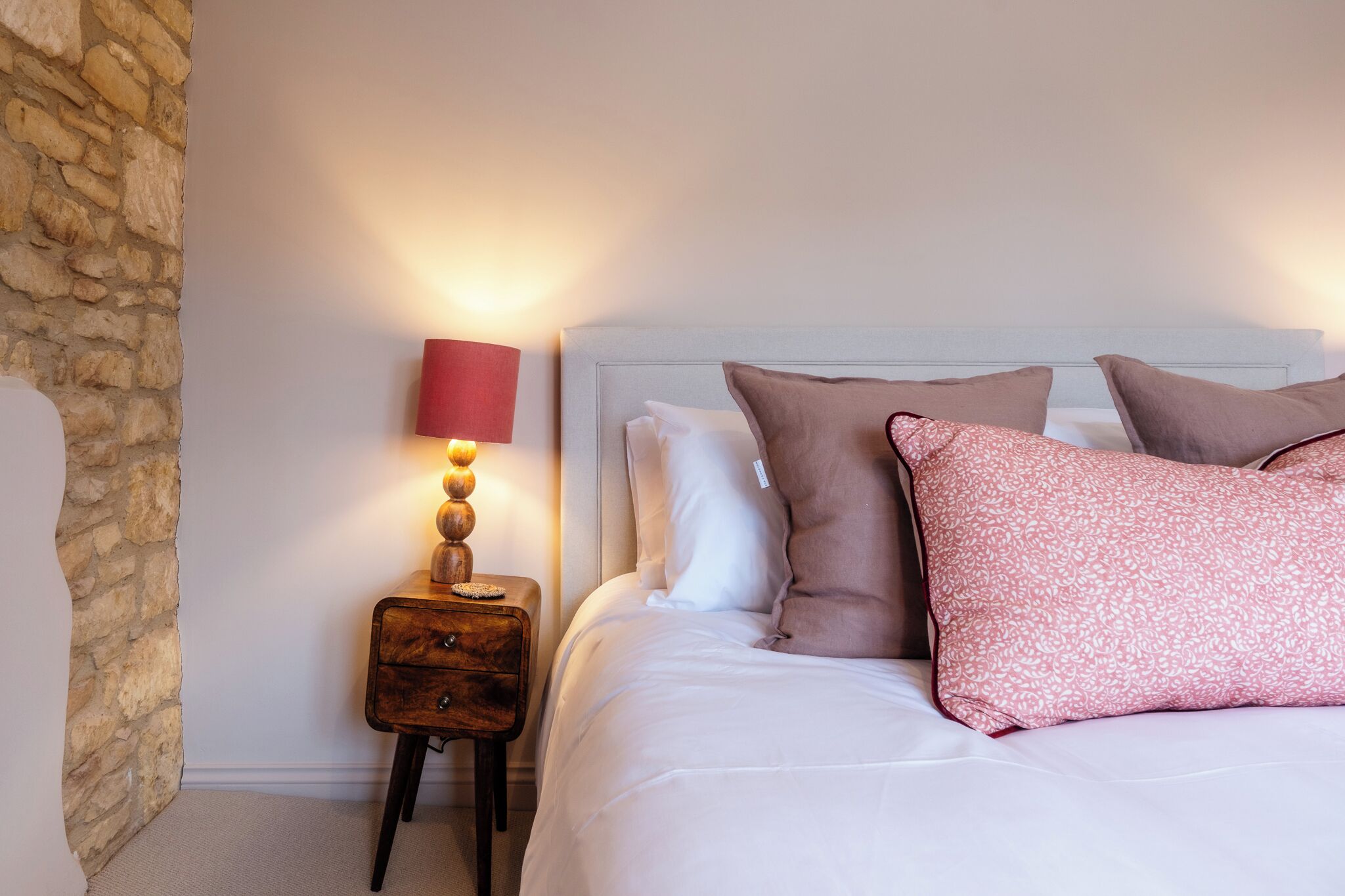 A neatly made bed with pillows, a bedside lamp, and a small wooden nightstand.