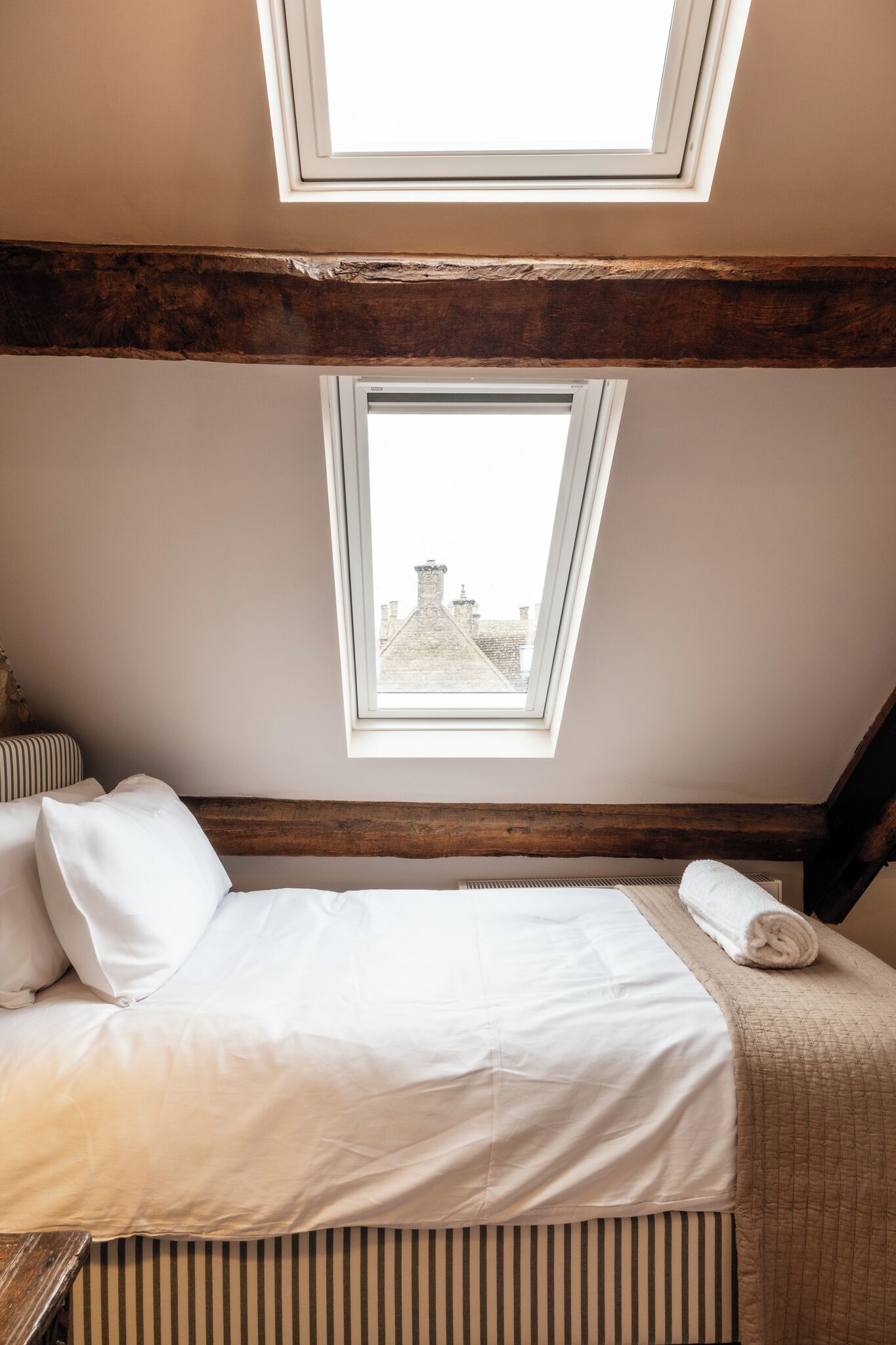 A bedroom with a bed, two skylights, and a view of buildings outside.