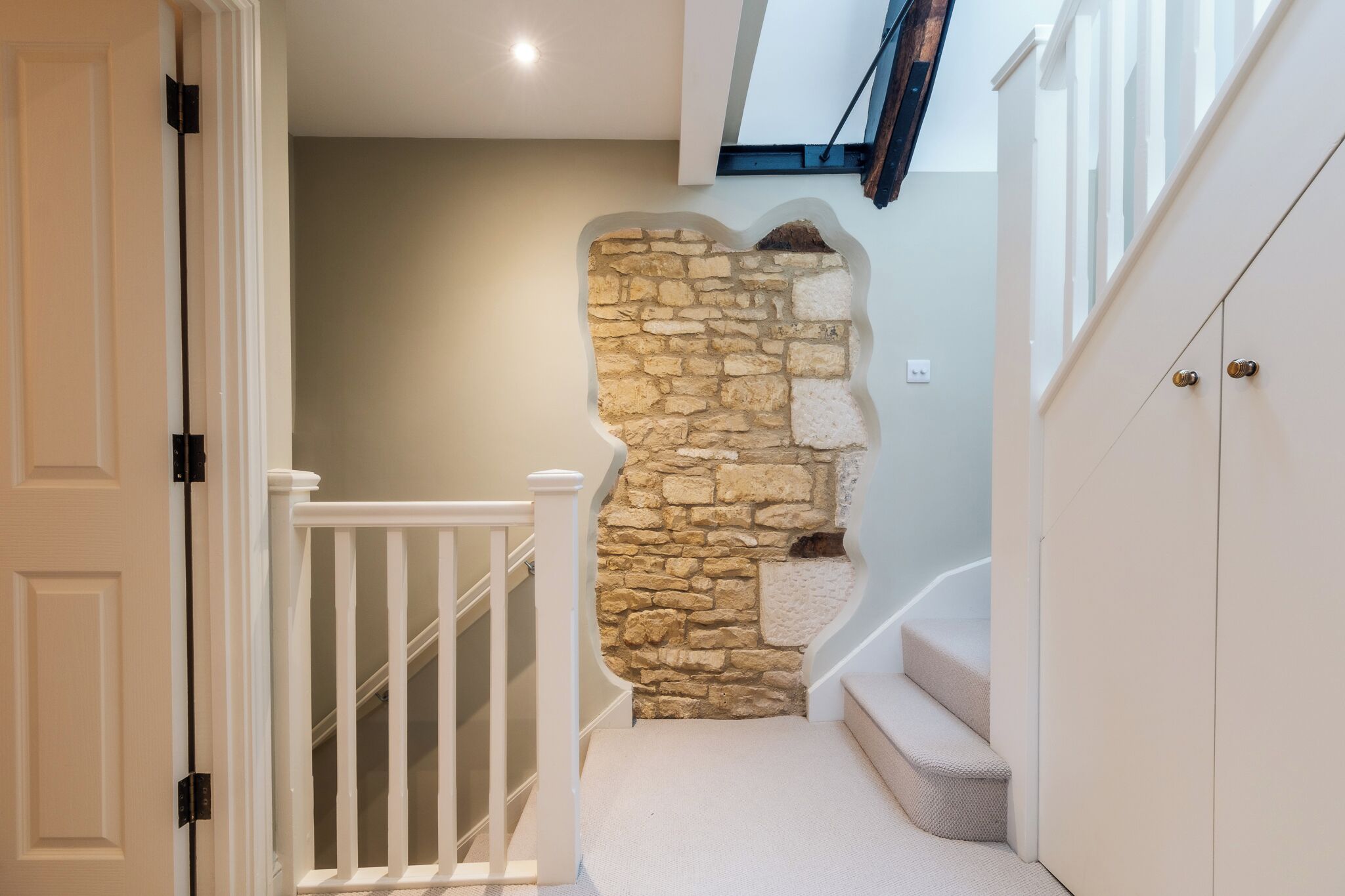 A staircase with a stone wall, white railings, and a carpeted landing.