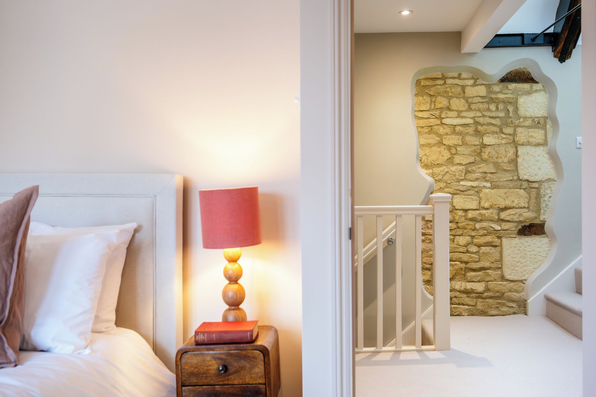 Une chambre à coucher avec un lit, une table de chevet, une lampe et un mur en pierre en arrière-plan.