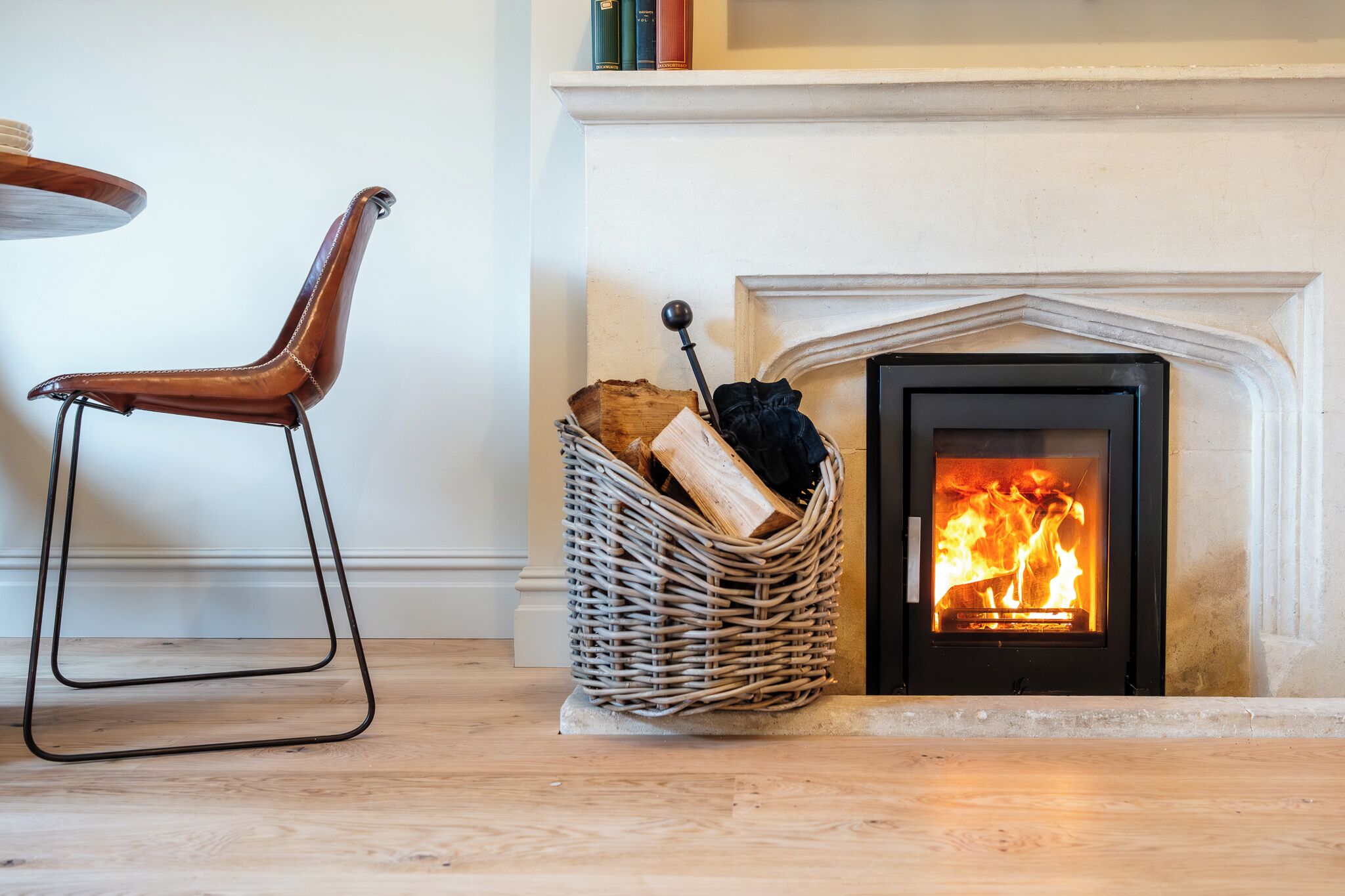 A fireplace with logs, a wicker basket, and a leather chair.
