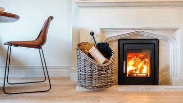 A fireplace with logs, a wicker basket, and a leather chair.