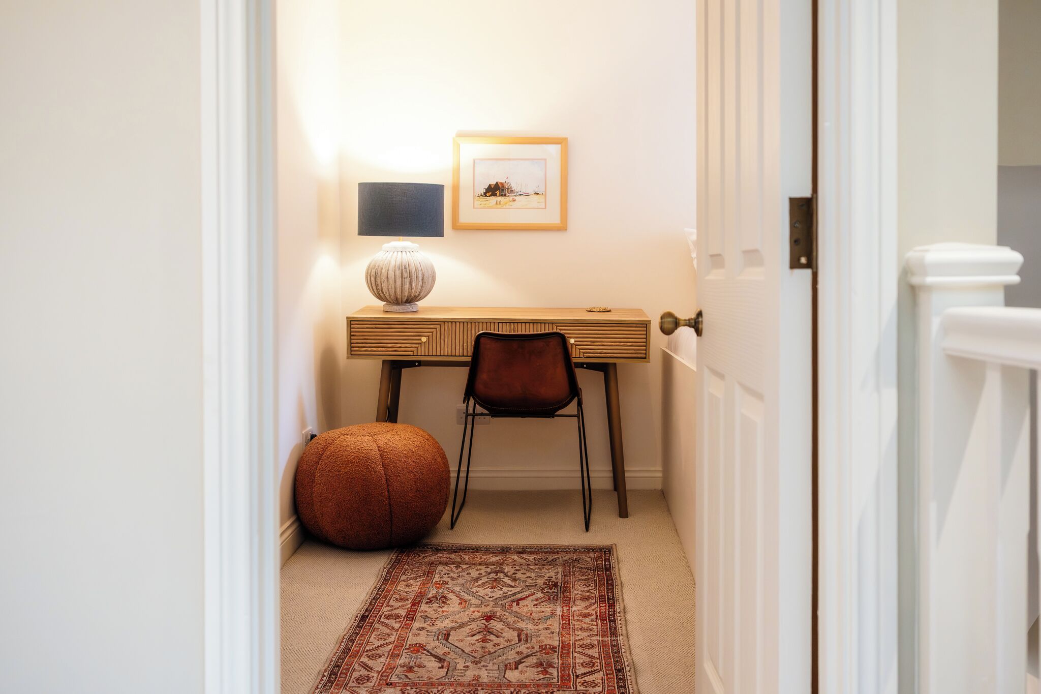 A small, neatly arranged office space with a desk, chair, rug, and a framed picture on the wall.