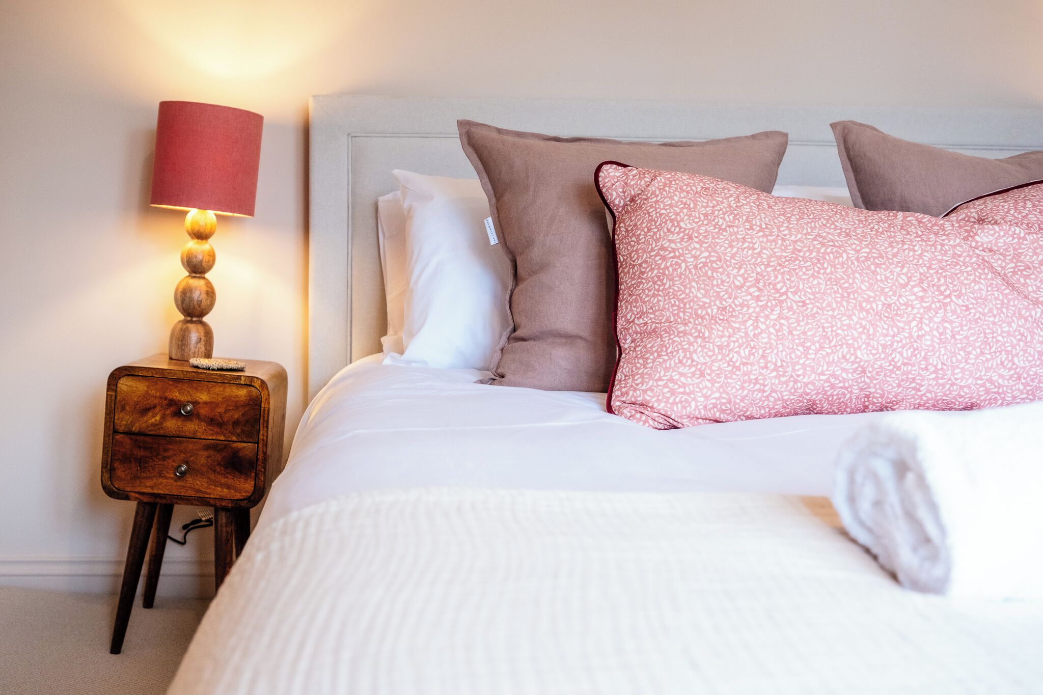 A neatly made bed with pillows, a bedside lamp, and a wooden nightstand.