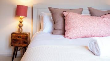 A neatly made bed with pillows, a bedside lamp, and a wooden nightstand.