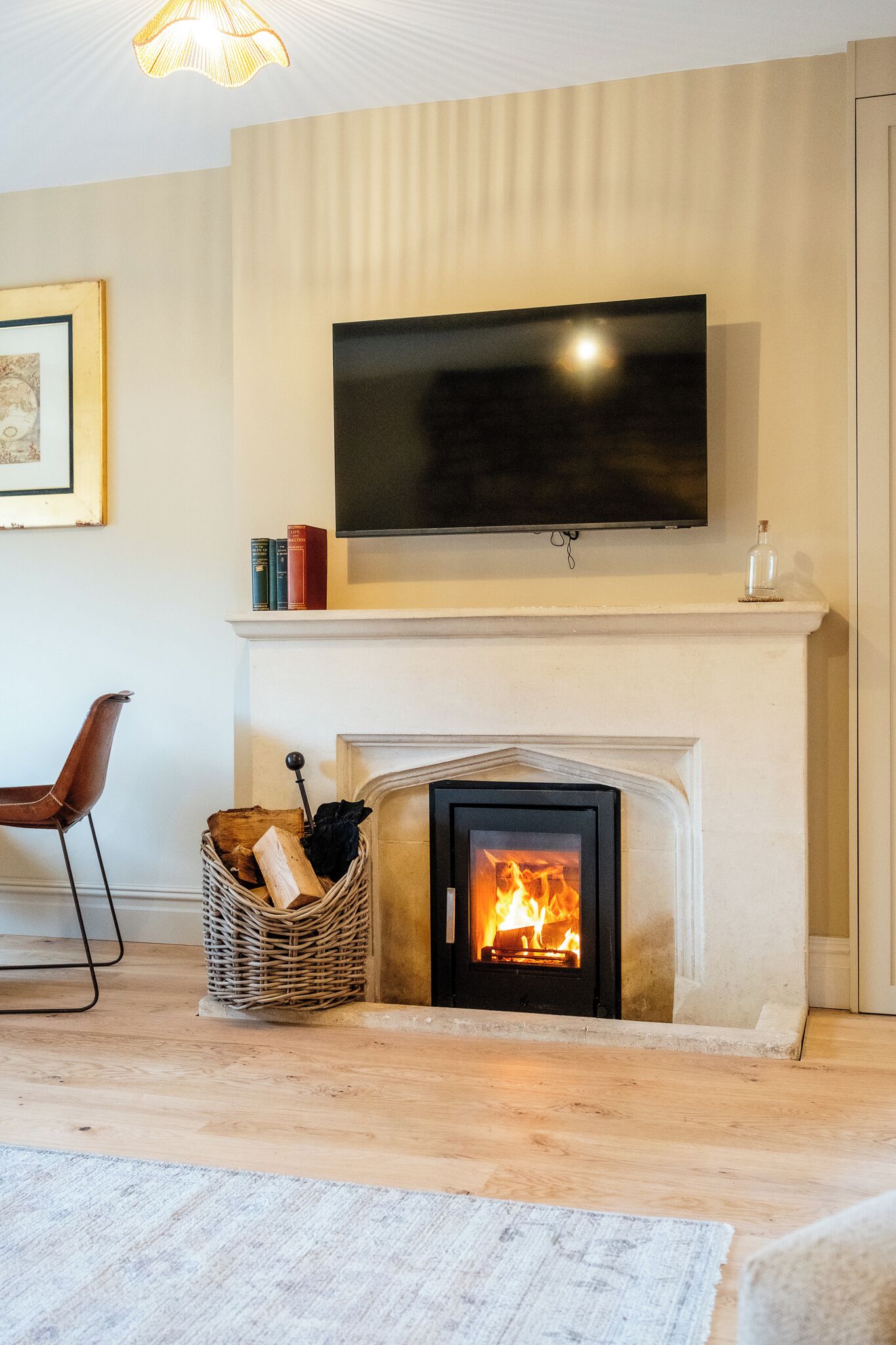 A living room with a fireplace, a television mounted above it, a chair, and a basket of firewood.