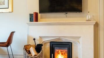 A living room with a fireplace, a television mounted above it, a chair, and a basket of firewood.