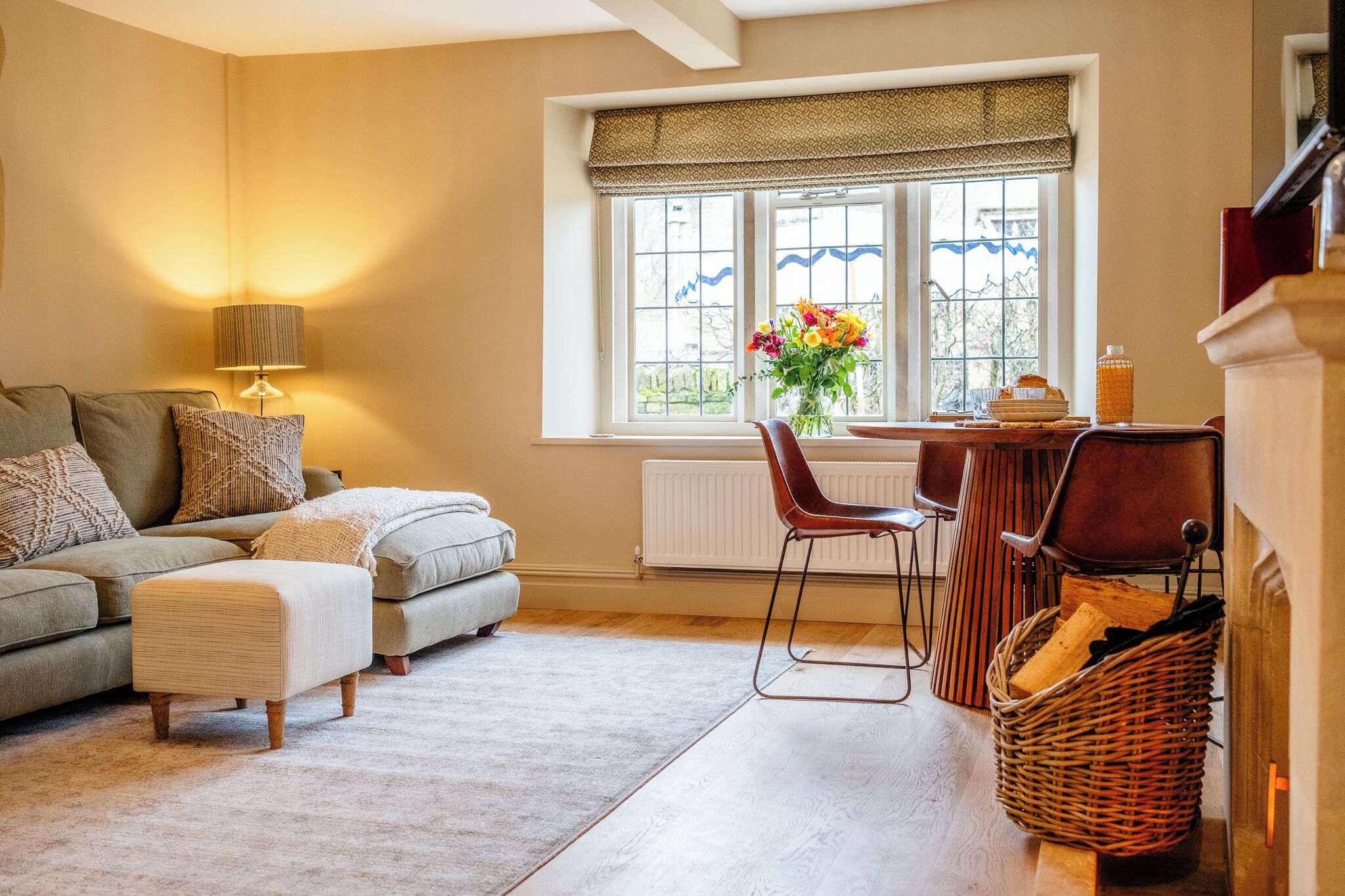 Een woonkamer met een bank, een voetenbankje, een lamp en een raam met uitzicht.