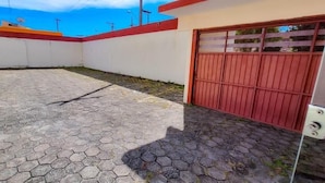 Une cour dallée, avec une porte rouge, un mur blanc et un toit rouge.