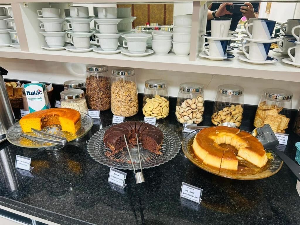 Ein Buffet mit verschiedenen Desserts und Snacks, darunter Kuchen und Kekse, sowie eine Auswahl an Tassen und Untertassen auf den Regalen darüber.