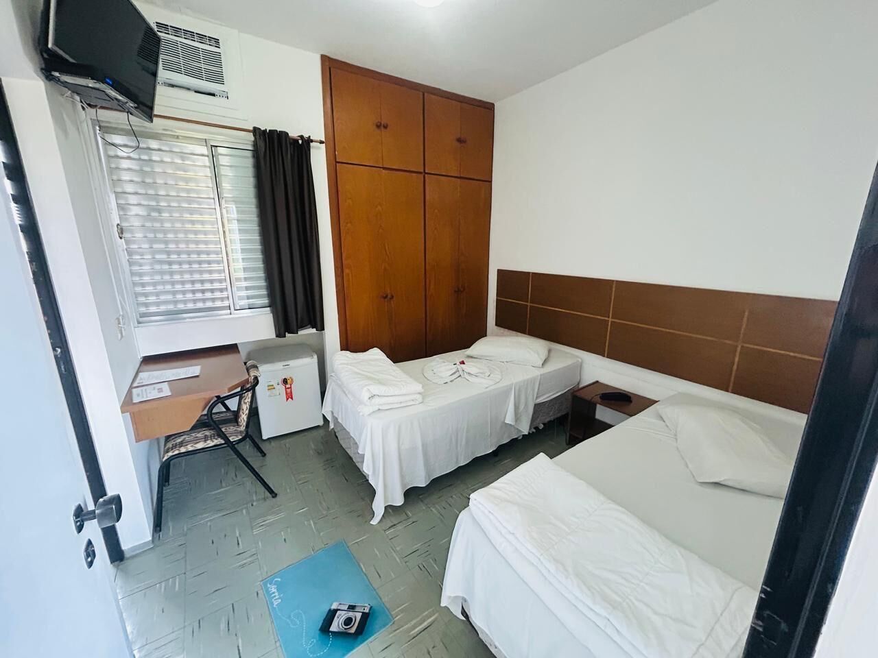 Habitación de hotel con dos camas, un escritorio, un armario y una ventana con cortinas.