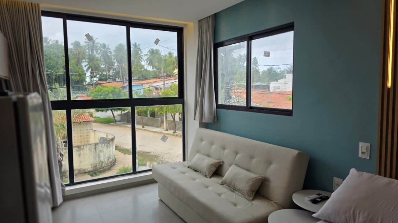 Una habitación con sofá, ventanas amplias y vistas a una zona residencial.