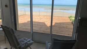 Een kamer met een groot raam met uitzicht op een strand. Er zijn twee stoelen en een kleine tafel.