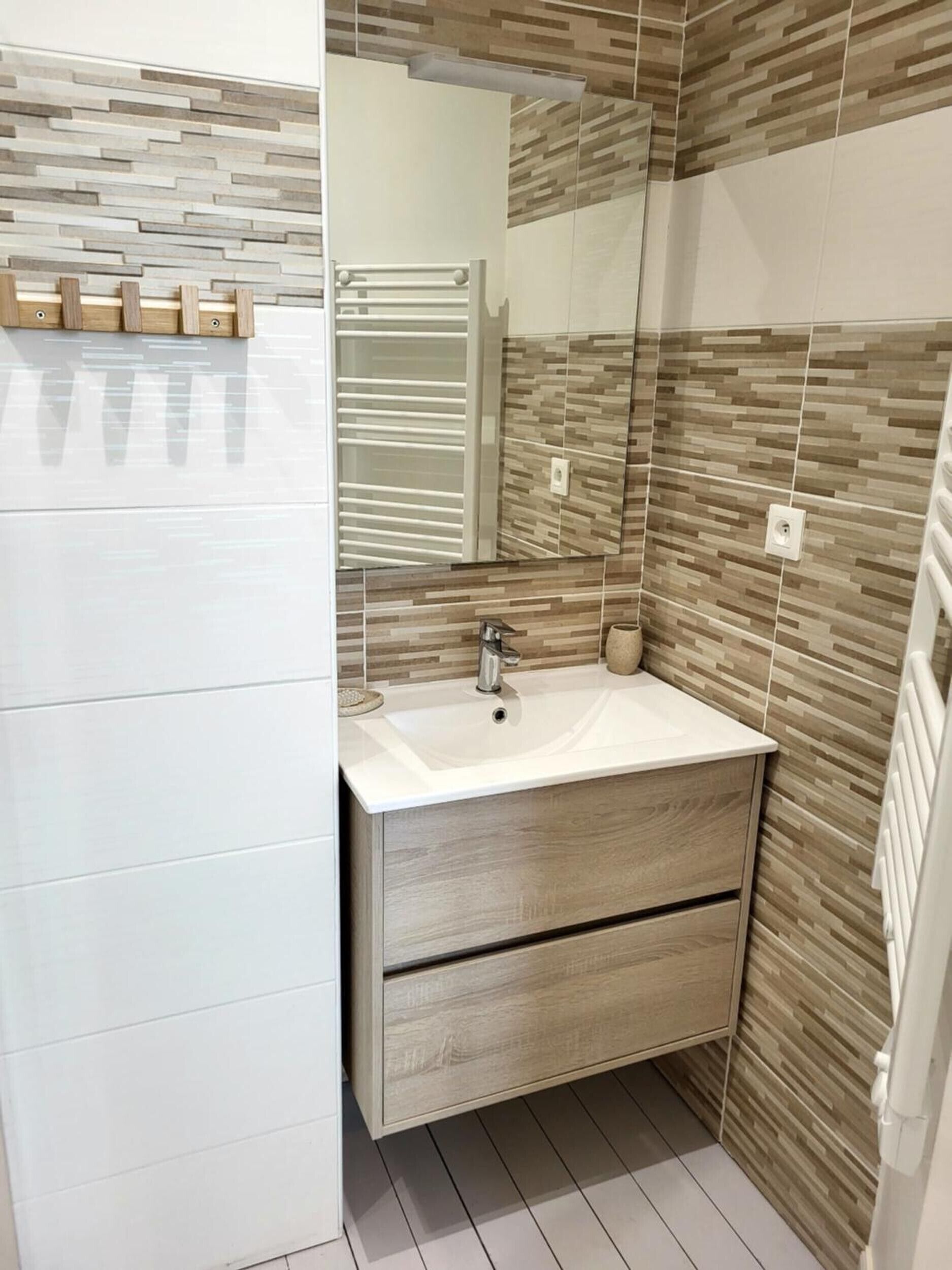 Een moderne badkamer met een witte wastafel, een houten opbergmeubel en een spiegel.