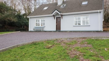 A single-story house with a gravel driveway, a front bench, and a door.