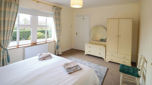 A bedroom with a bed, a dresser, a mirror, a wardrobe, and a window with curtains. - Lugdine Lodge (Glengarriff)