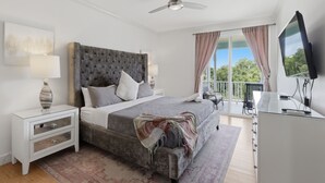 A bedroom with a bed, nightstand, TV, and a balcony with curtains. - New! Luxury Reunion Villa | Theater • Pool • Game Room (Kissimmee)