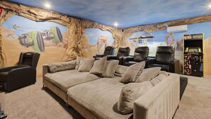 A room with a large sofa, massage chairs, and a wall mural depicting a desert scene. - New! Luxury Reunion Villa | Theater • Pool • Game Room (Kissimmee)