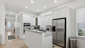 A modern kitchen with white cabinetry, stainless steel appliances, and a granite countertop island. - New! Luxury Reunion Villa | Theater • Pool • Game Room (Kissimmee)