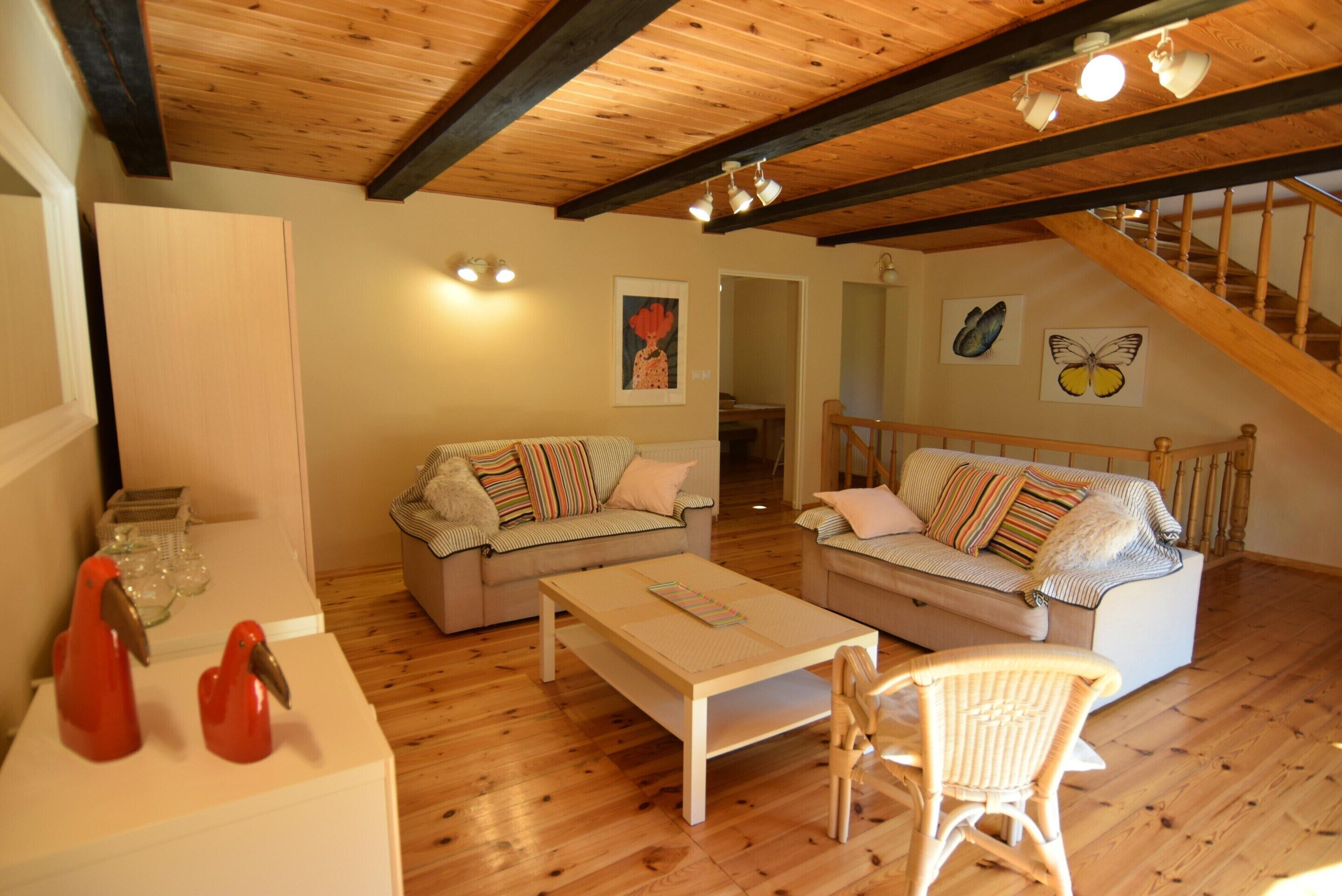 Un salón con piso de madera, dos sofás, una mesa de centro y un sillón de mimbre.