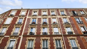Un immeuble à plusieurs étages, doté d’une façade symétrique, de nombreuses fenêtres avec volets et de balcons ornés de garde-corps en fer forgé.