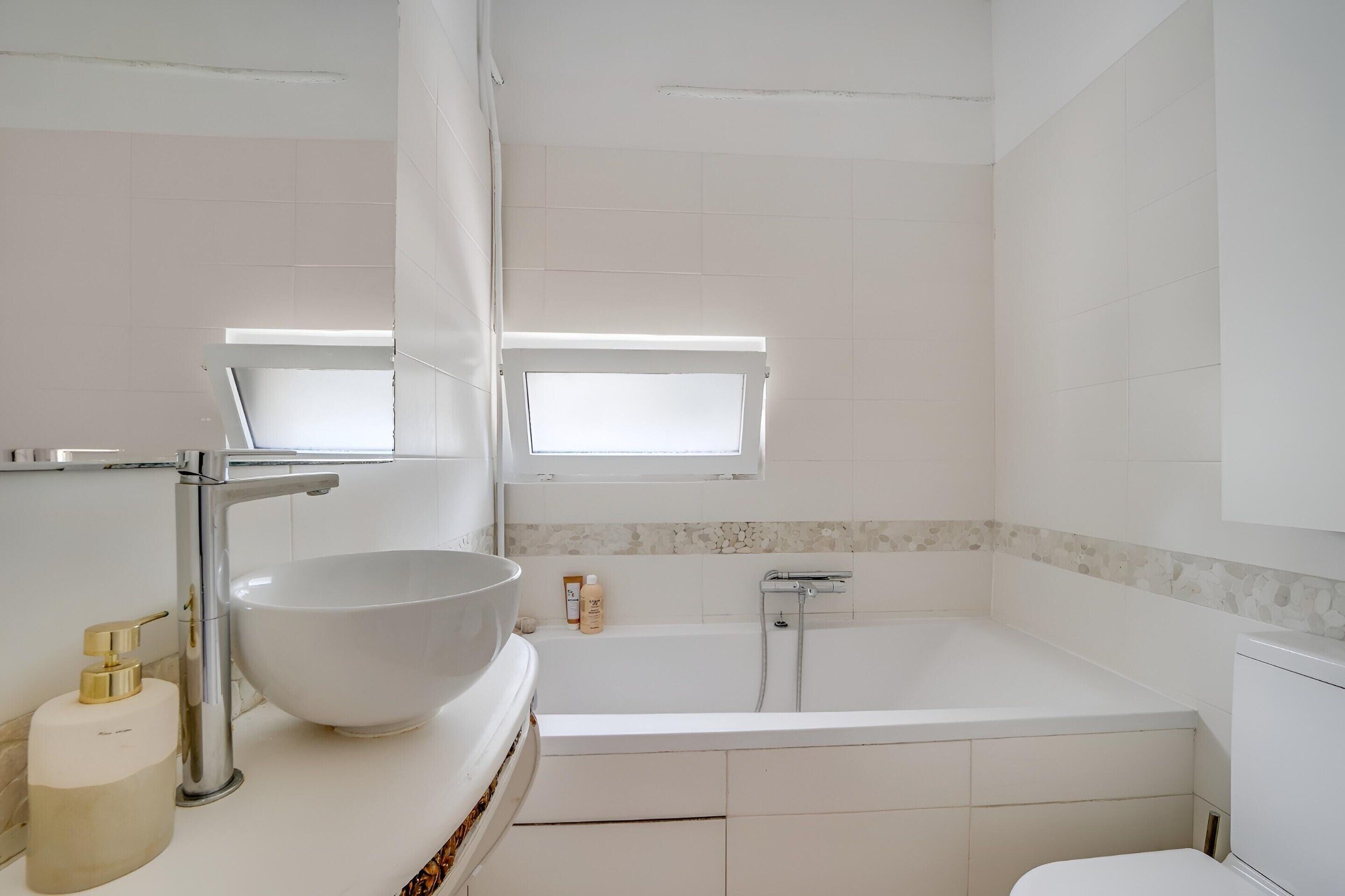A modern bathroom with a white sink, a bathtub, and a window above the sink.