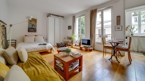 Une pièce bien éclairée, comprenant un lit, un canapé, une table basse en bois, un téléviseur et un coin repas avec des chaises.