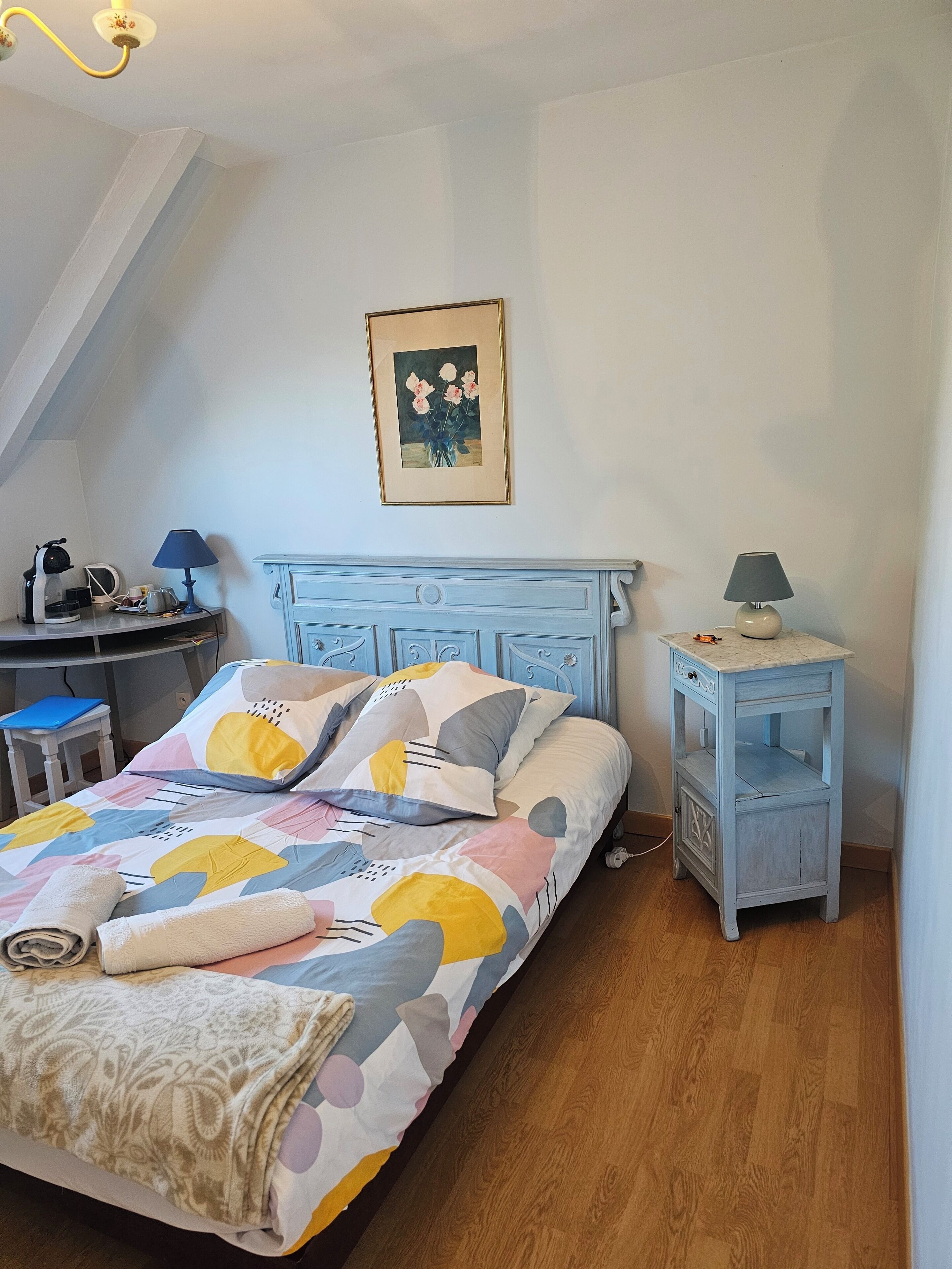 Une chambre à coucher avec un lit, un bureau, une chaise, une lampe et un tableau au mur.