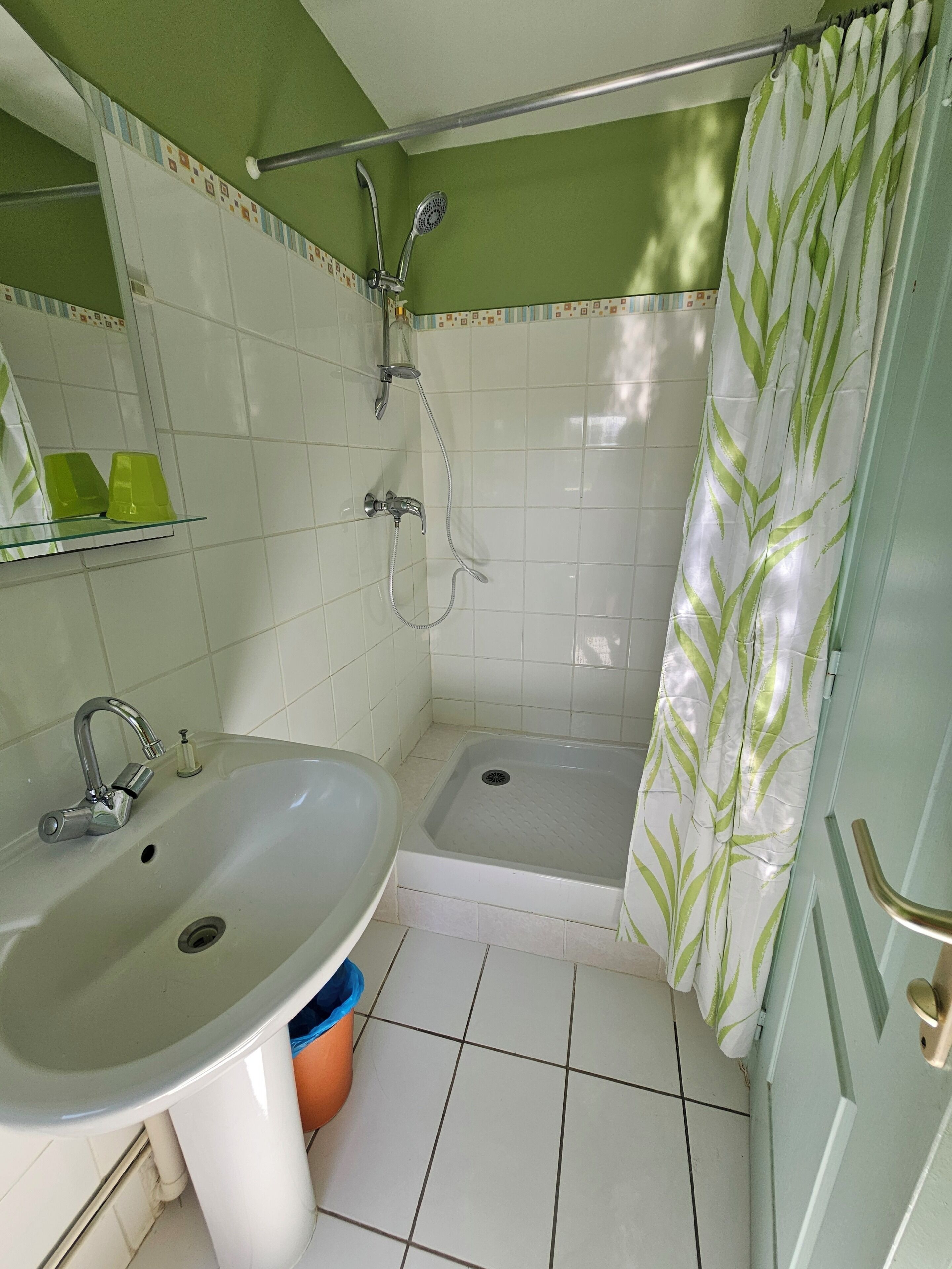 Een badkamer met een wastafel, douche en een douchegedeelte betegeld met groen.