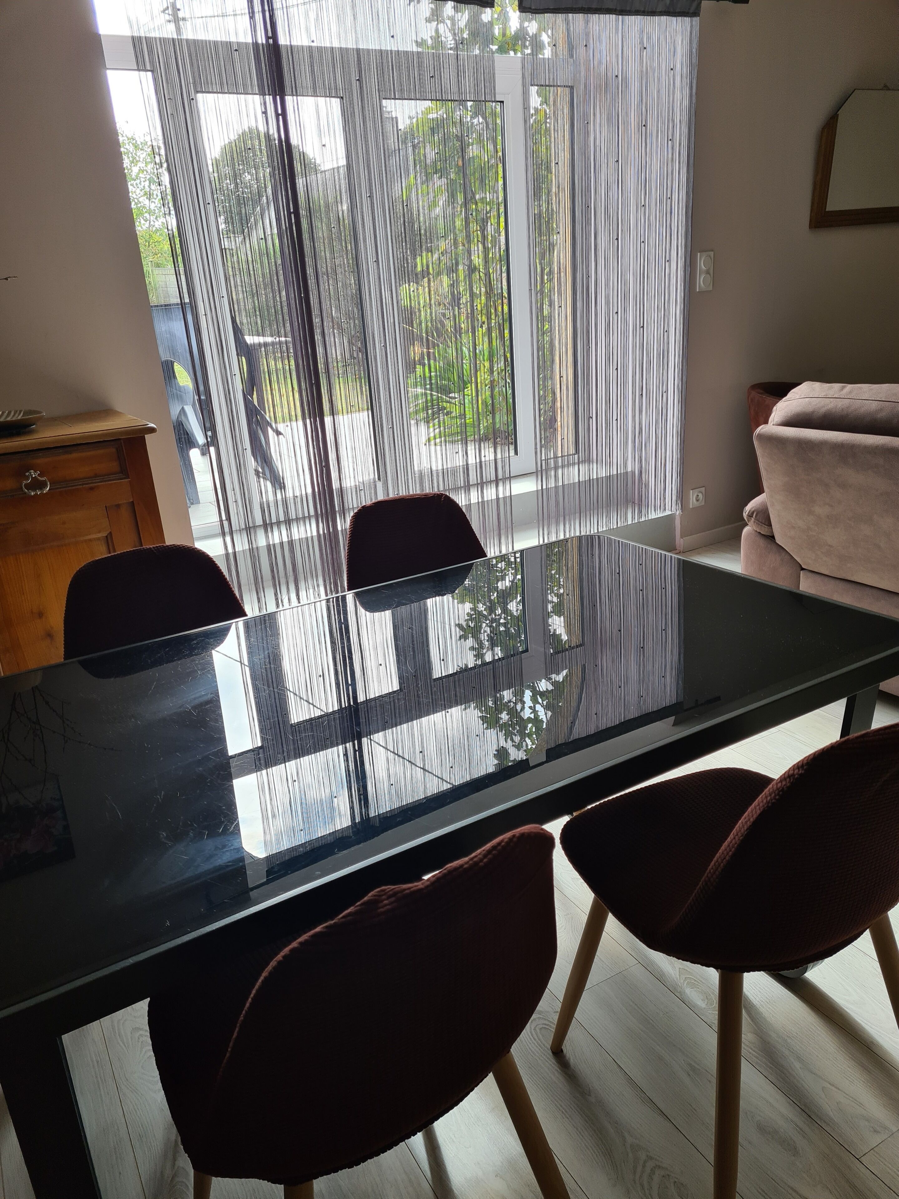 Un comedor moderno con una mesa de vidrio, dos sillas, un mueble de madera y un sofá.