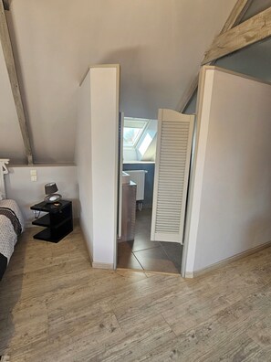 A bedroom with a sloped ceiling, a skylight, a bed, a bedside table with a lamp, and a radiator. - Les Closeries du Golfe (Theix-Noyalo)