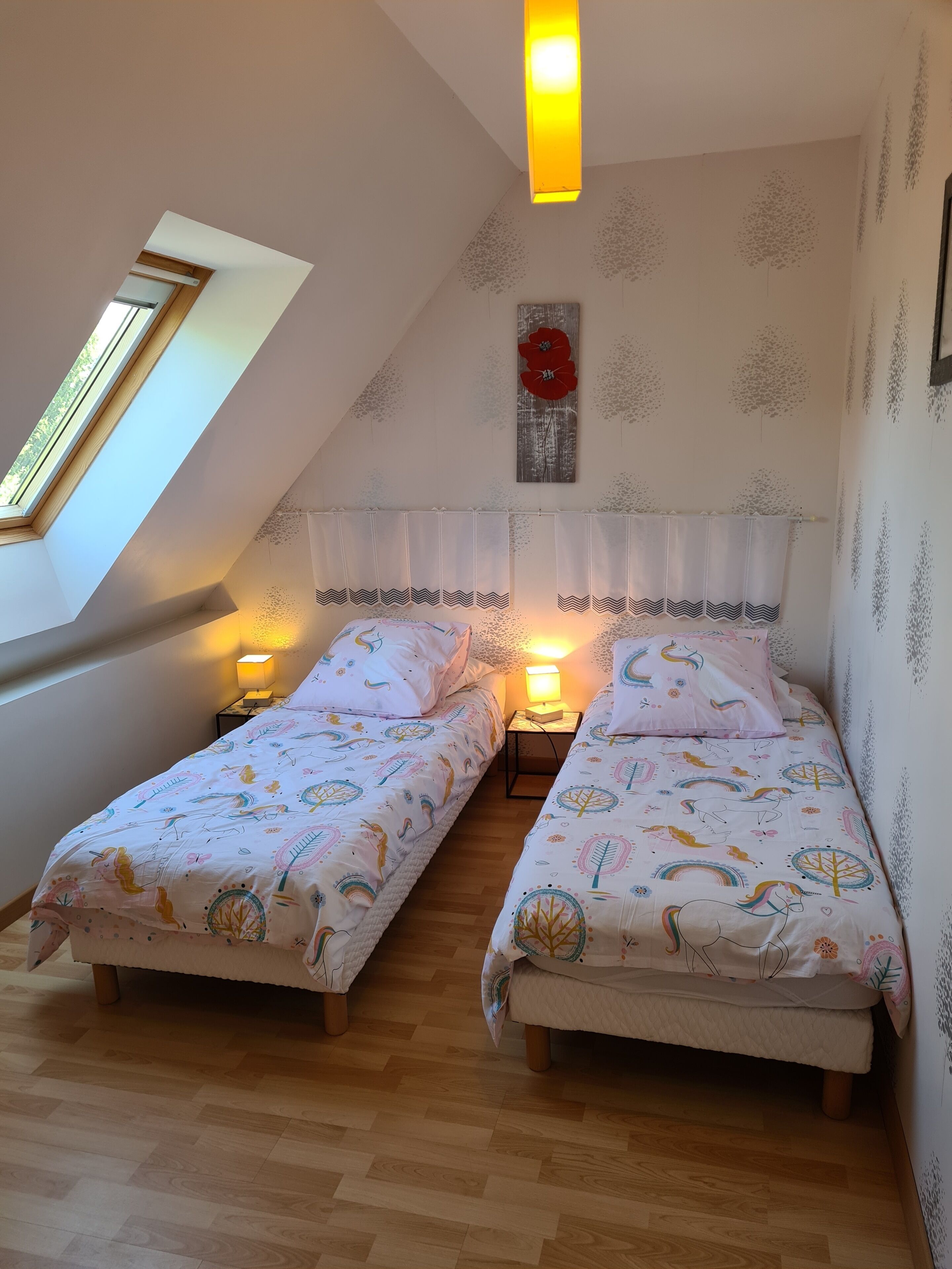 Un dormitorio con dos camas, un tragaluz, una decoración floral roja y una pared con motivos de árboles.
