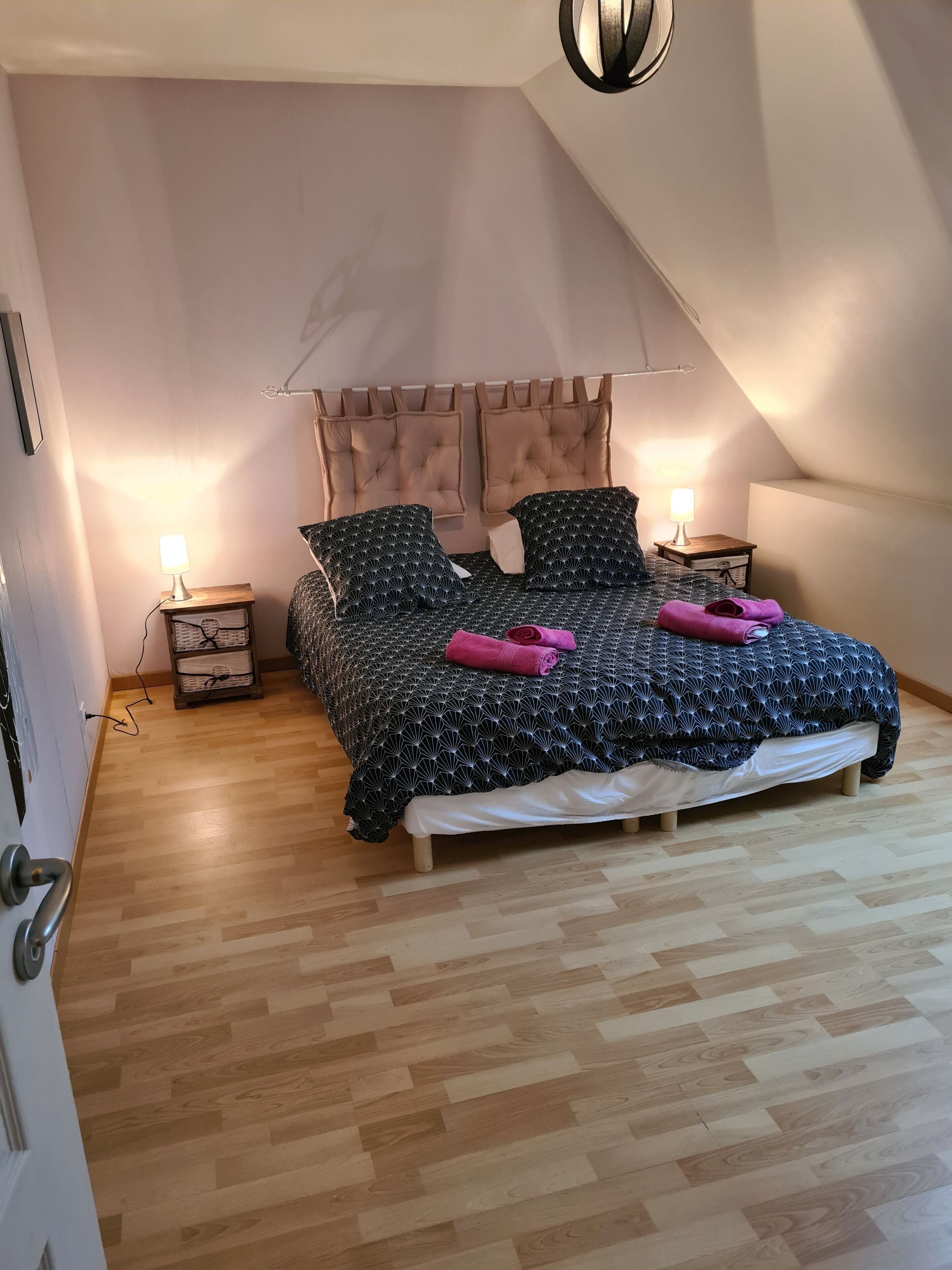 Une chambre à coucher avec un lit, deux tables de chevet, une lampe, un plancher en bois et un plafond en pente.