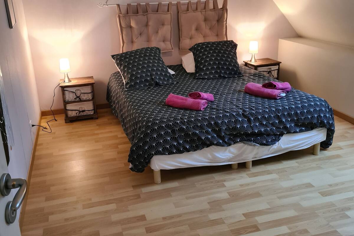 A bedroom with a bed, two bedside tables, a lamp, a wooden floor, and a sloped ceiling.