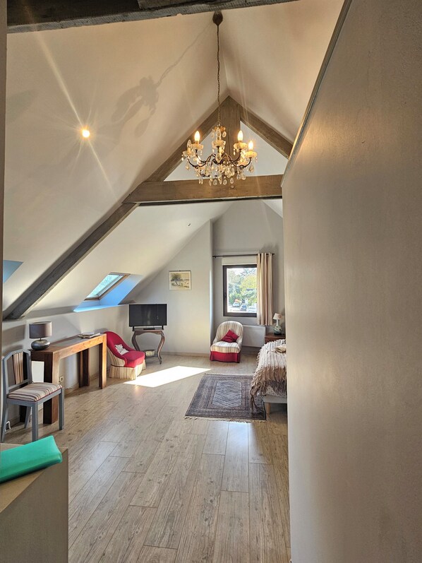 A spacious loft with a sloped ceiling, a chandelier, a television, a red chair, and a view of the outdoors. - Les Closeries du Golfe (Theix-Noyalo)