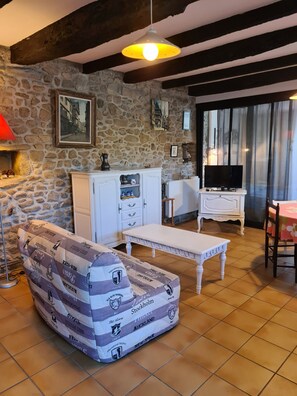 A living room with a stone wall, a white cabinet, a television, and a patterned sofa. - Les Closeries du Golfe (Theix-Noyalo)
