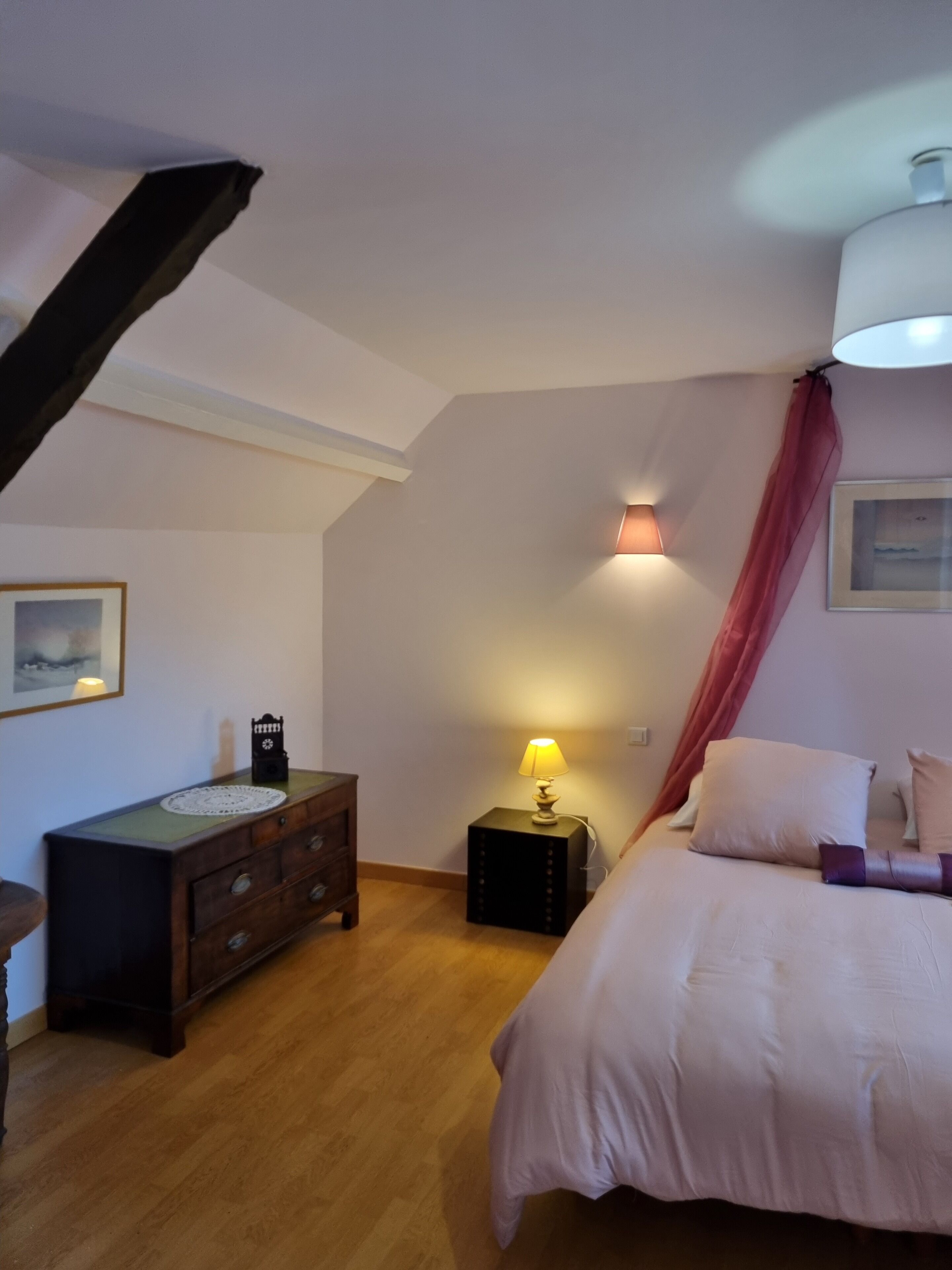 Un dormitorio con cama, cómoda, mesita de noche con lámpara, un cuadro en la pared y ventilador de techo.