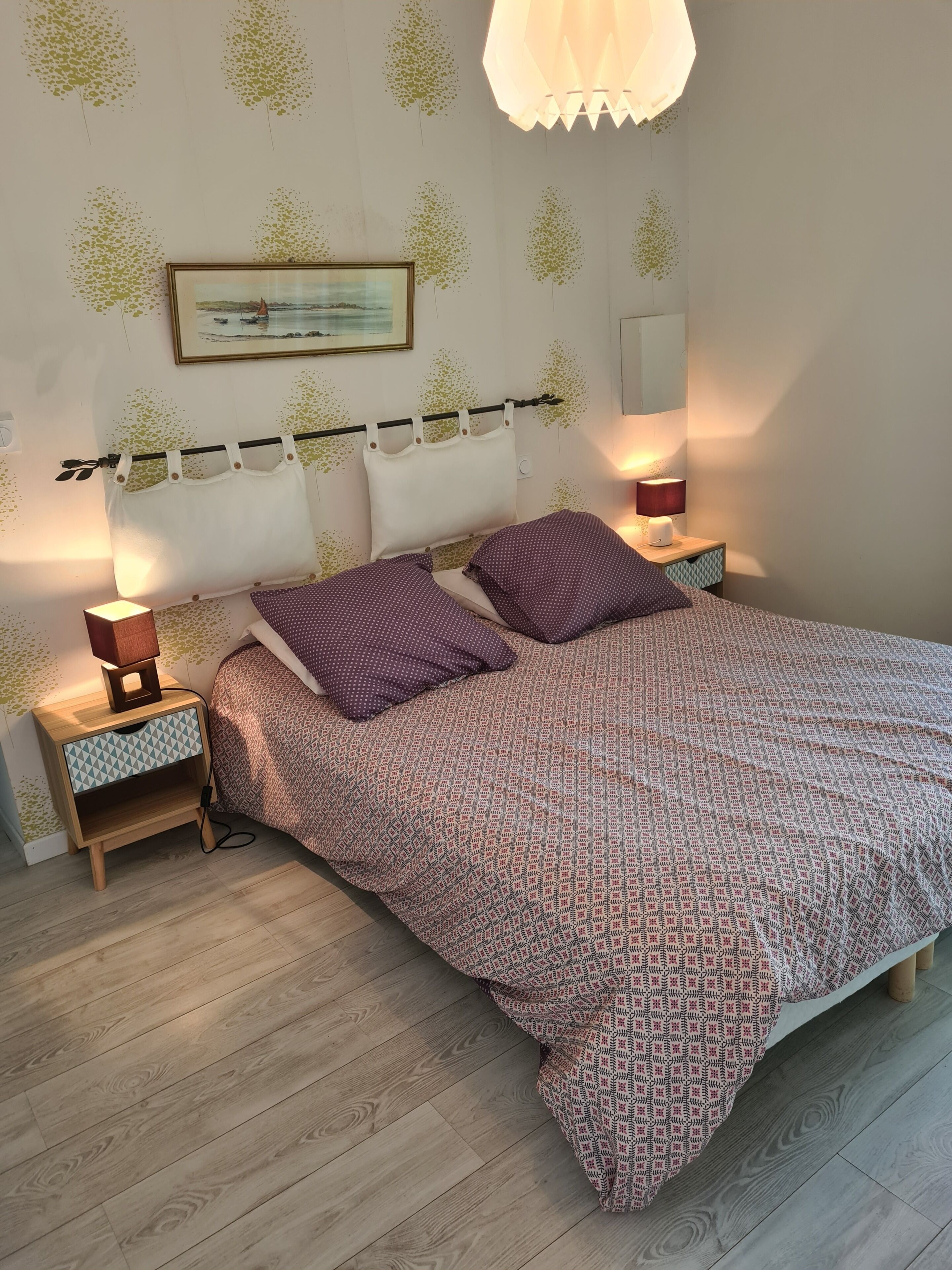A bedroom with a bed, two bedside tables, a nightstand, a wall-mounted lamp, and a framed picture.