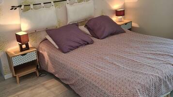 A bedroom with a bed, two bedside tables, a nightstand, a wall-mounted lamp, and a painting.
