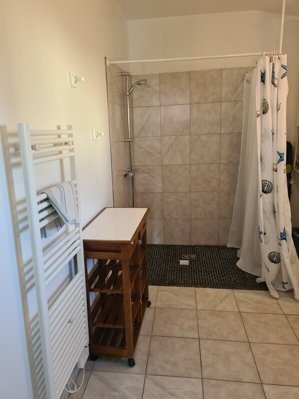 Une salle de bain avec une douche, un porte-serviettes, une étagère en bois et un carrelage au sol.