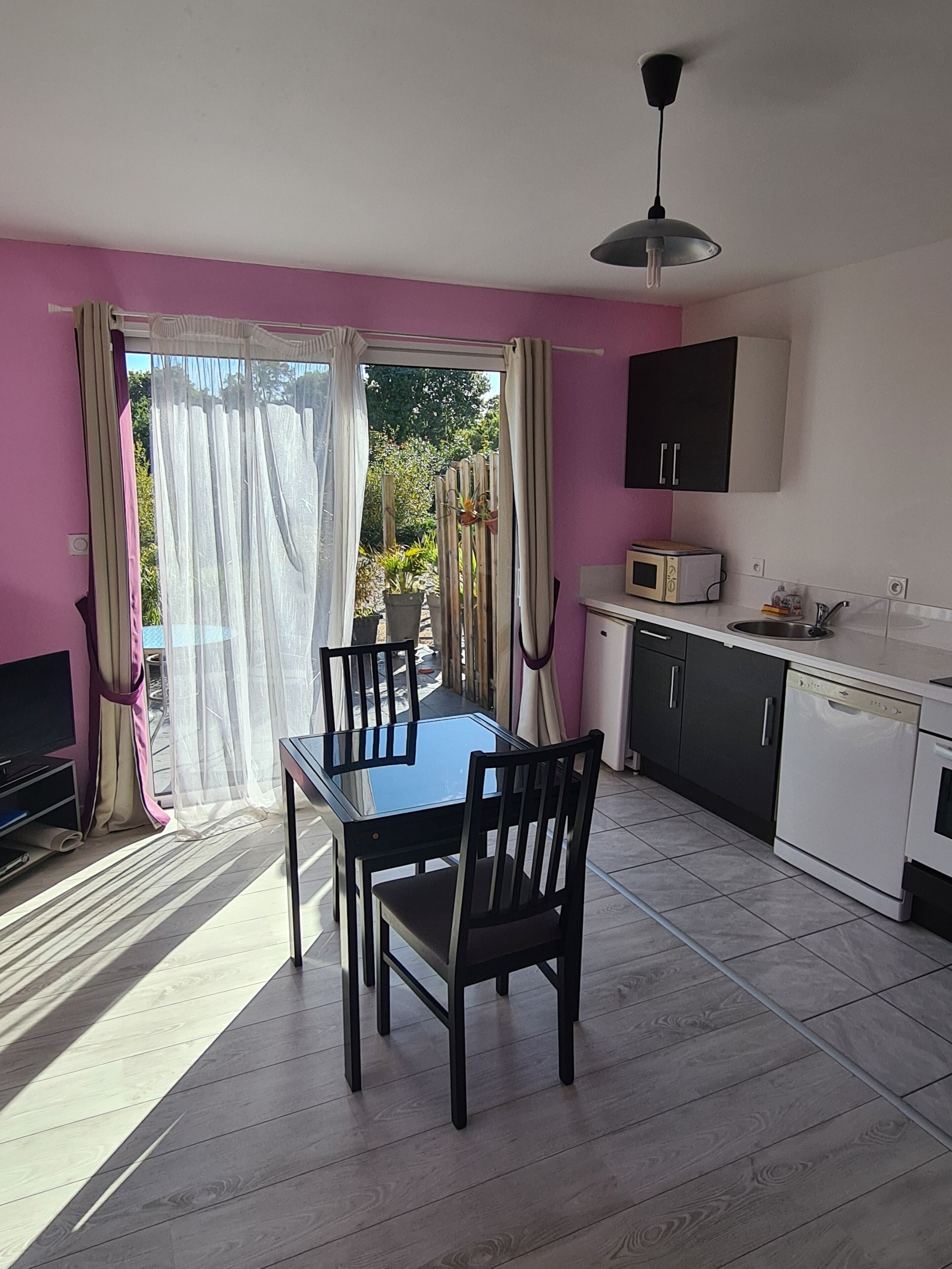 A room with a dining table, chairs, a TV, a microwave, and a sink.