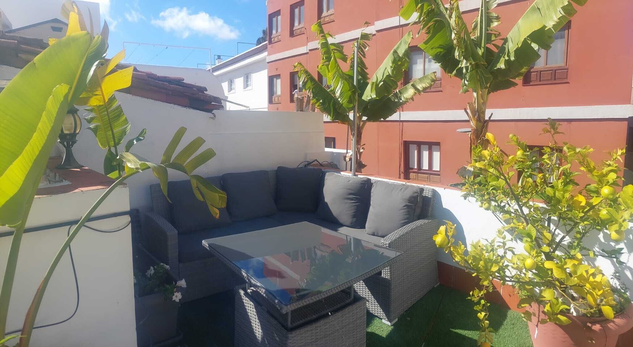 Un patio con una mesa de vidrio y un sofá de color oscuro.