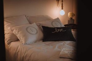 A bed with two pillows, one with a monogram and another with the word 'love' written on it.