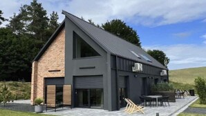 Una casa moderna con techo inclinado, ventanas amplias y un patio con mobiliario exterior.