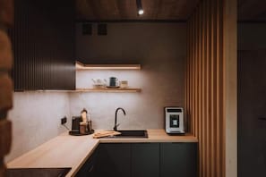 A compact kitchen with a sink, a coffee machine, and a small shelf with cups and a teapot.