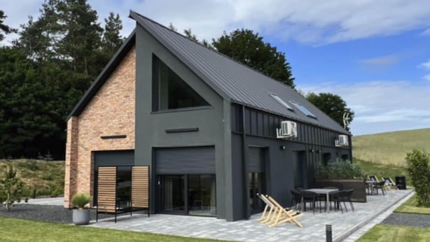 A modern house with a sloped roof, large windows, and a patio with outdoor furniture. - Large holiday home with a jacuzzi on the terrace (Kościerzyna)